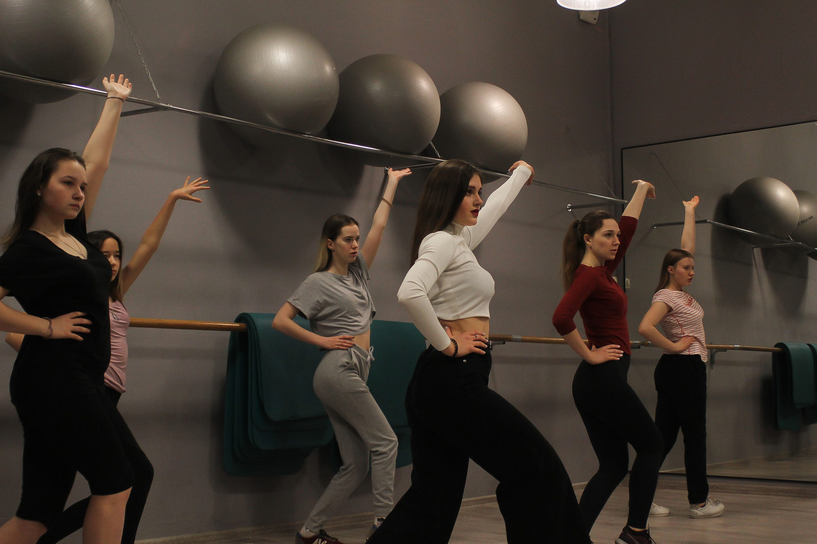Group of women practicing dance moves in a modern studio with exercise balls and mirrors.